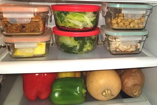 shelf in fridge with vegetables and leftovers in glass containers on top of clear fridge shelf liner