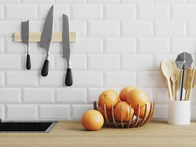 minimalist kitchen knives, utensils, bowl of oranges on wooden countertop with white tiled wall