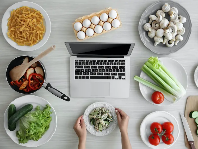 minimalist meal planning top view woman's hands on salad bowl in front of laptop and food