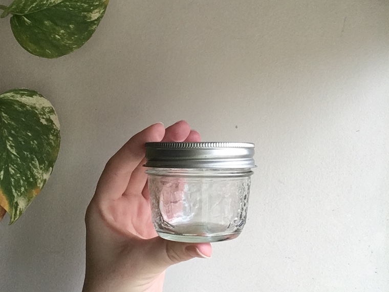 4oz small mason jar held by white hand with background of off white and green leaves