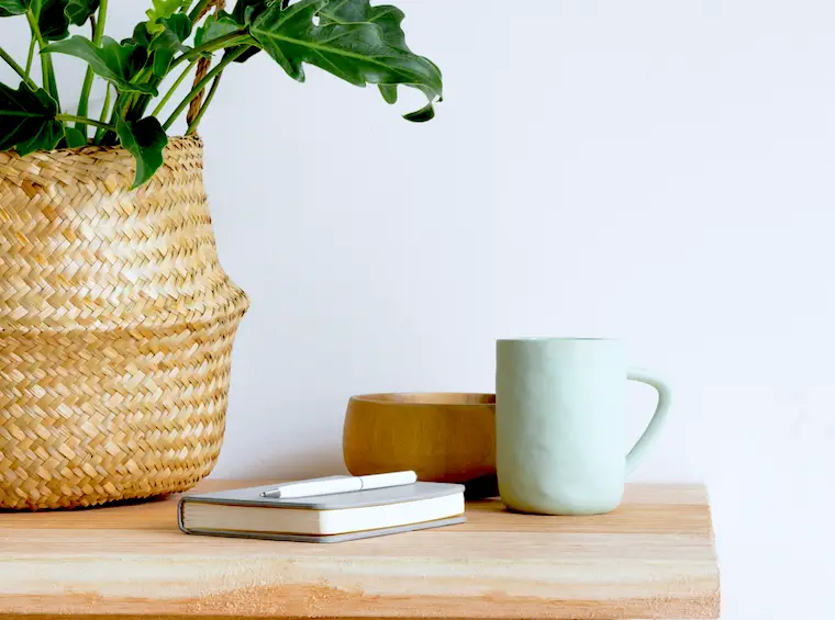 minimalist coffee mug on wood table with notebook and plant